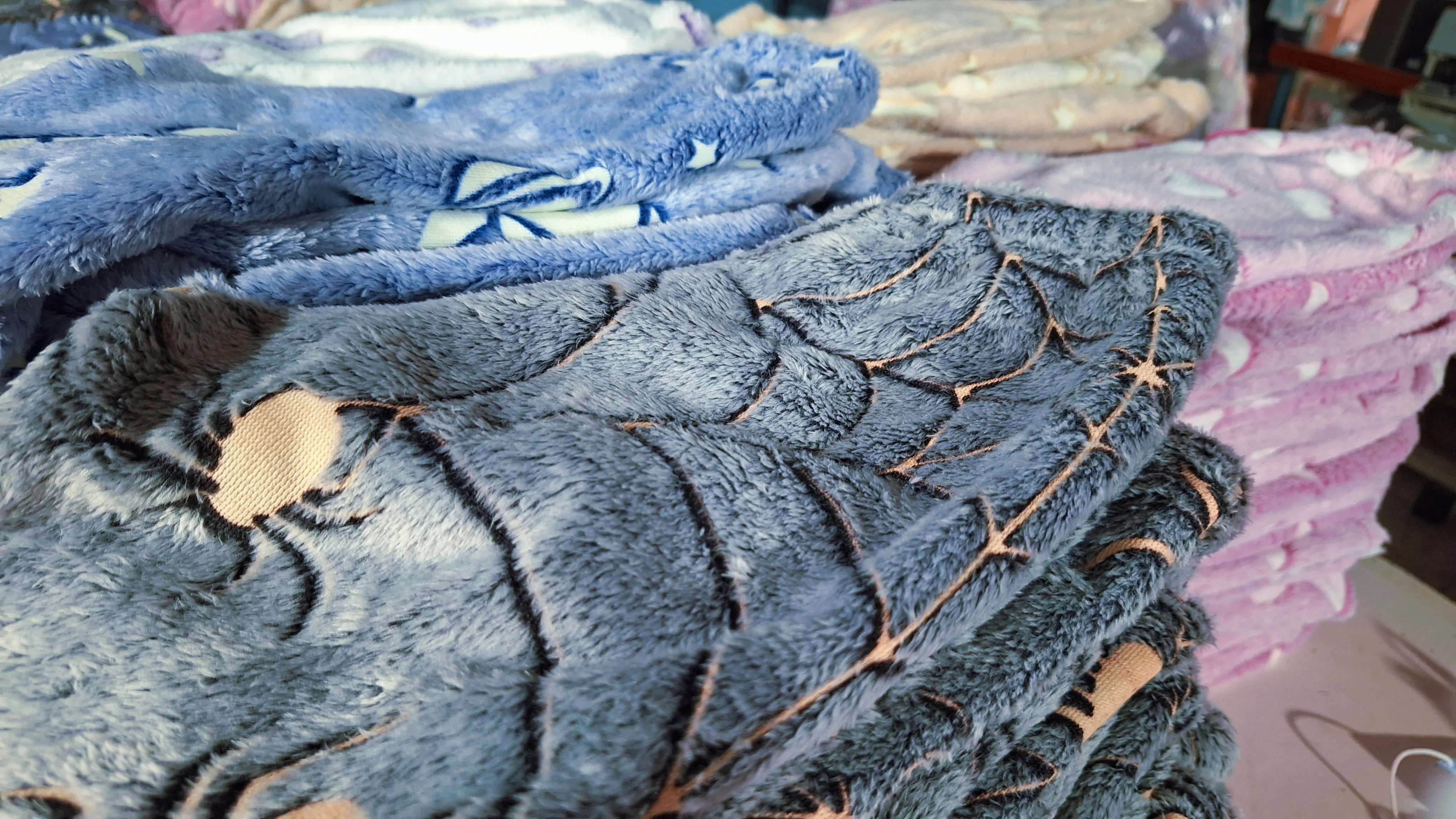 Mantas y prendas de polar soft dobladas en azul, gris y rosa, con texturas estampadas.